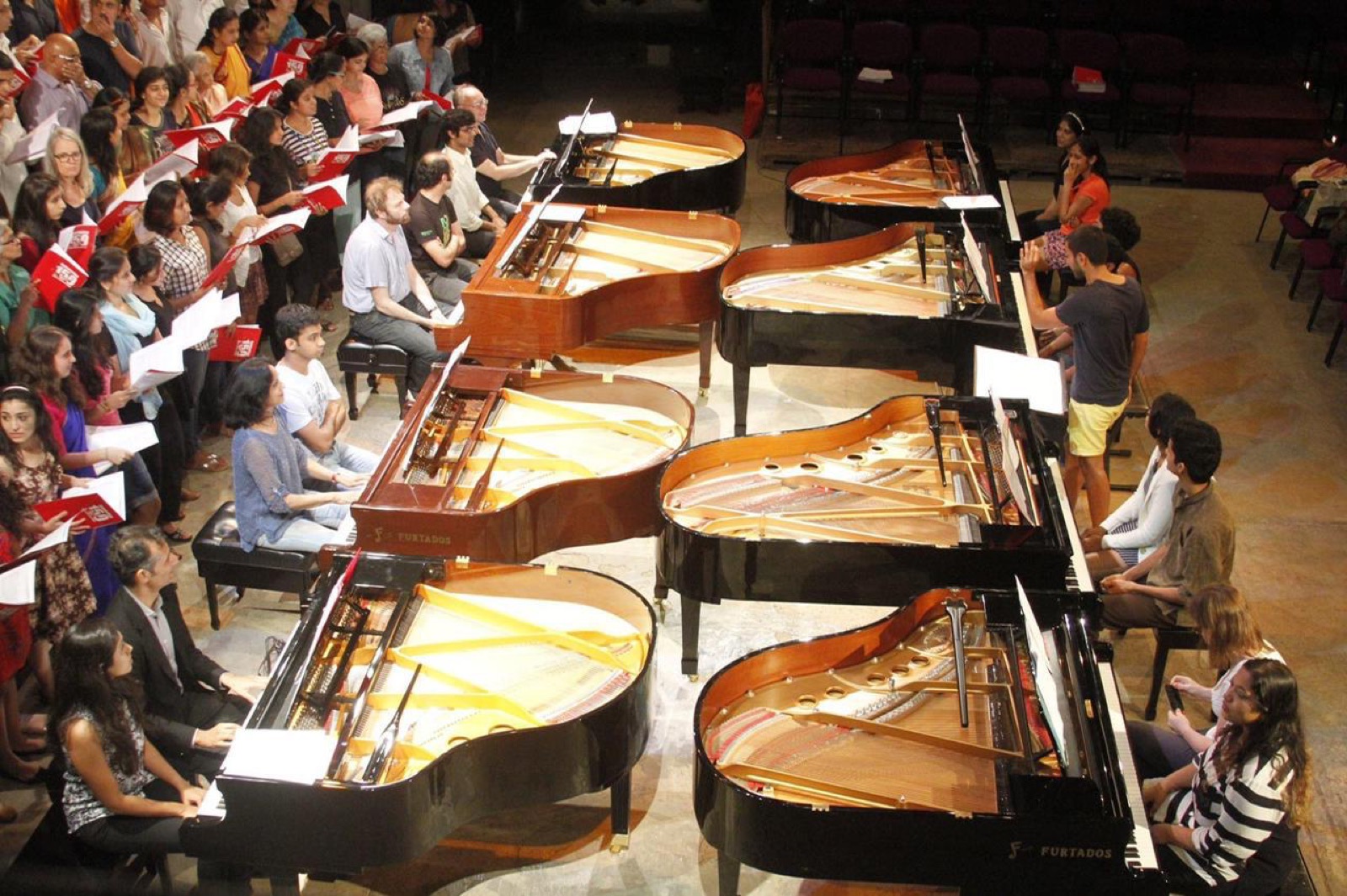 Multiple grand pianos arranged on stage at the Con Brio festival, with performers and an audience